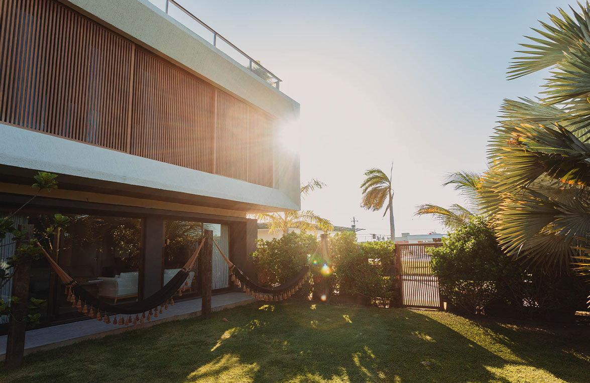 Fachada da Casa Lençóis com brises de madeira, jardim gramado e rede ao entardecer