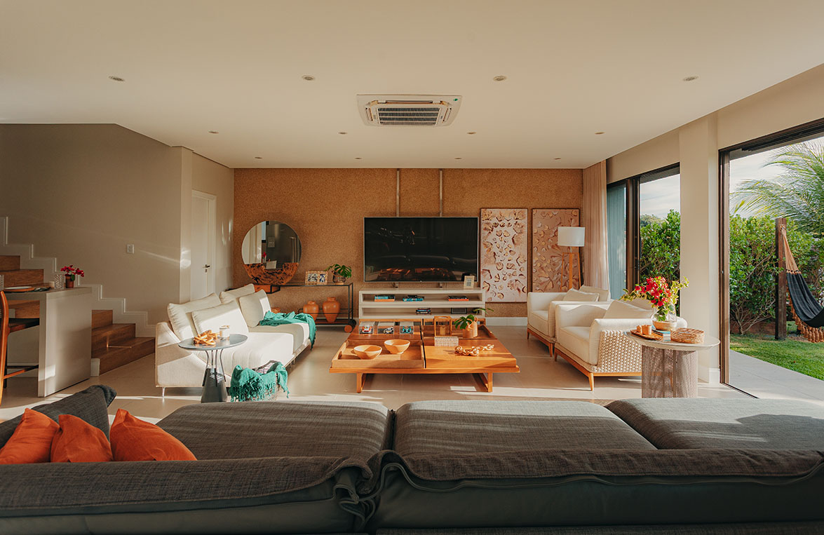 Sala de estar ampla com sofás, mesa de centro em madeira, TV e varanda aberta para o jardim