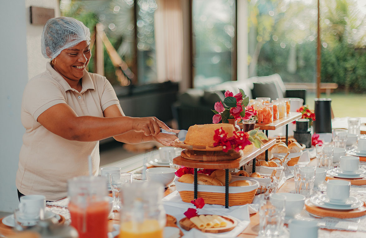 Cozinheira sorridente preparando mesa de café da manhã com bolos, pães e frutas frescas
