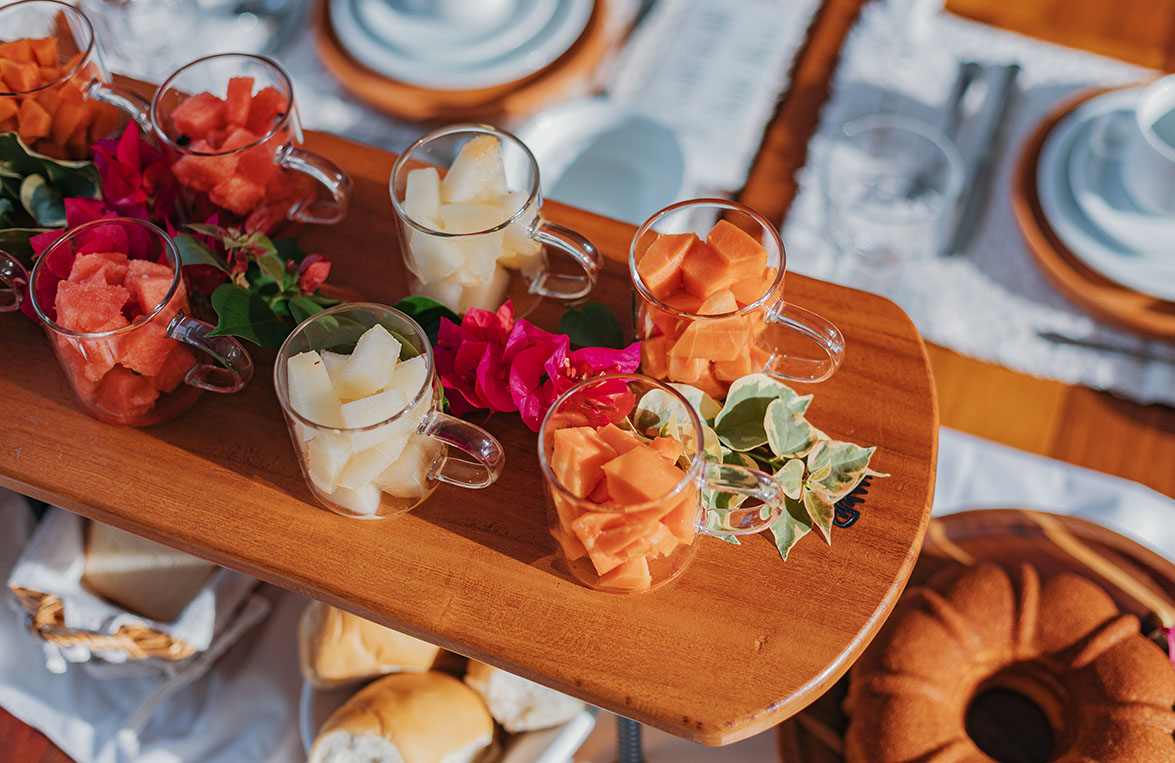 Tábua de frutas frescas cortadas em copinhos com flores de buganvília na mesa do café