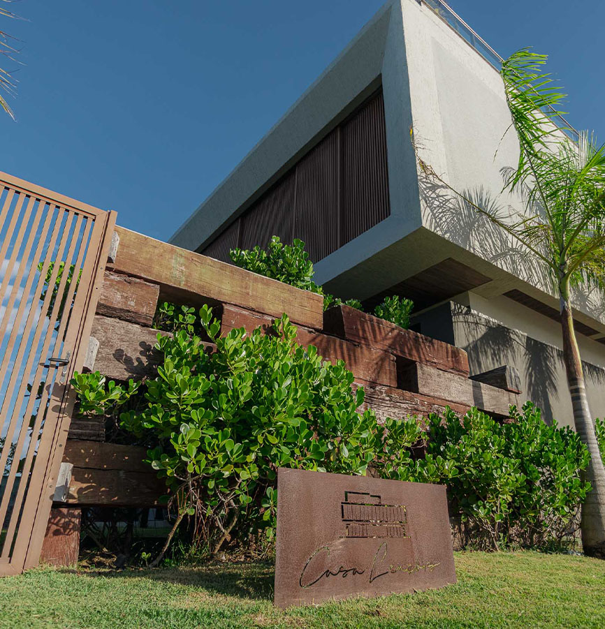 Entrada da Casa Lençóis com muro de madeira de demolição, vegetação e placa