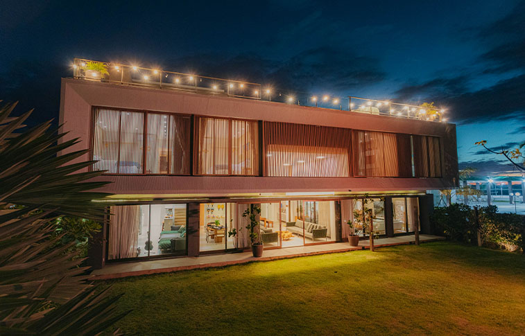 Fachada da Casa Lençóis iluminada à noite com arquitetura contemporânea e jardim